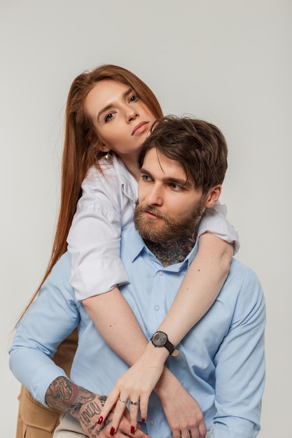 Fashionable trendy hipster couple beautiful woman and fashion handsome brutal man in stylish shirt sits and hug on a white background in studio