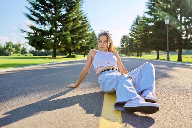 公園の道路に座っているファッショナブルなトレンディな10代の流行に敏感な女性
