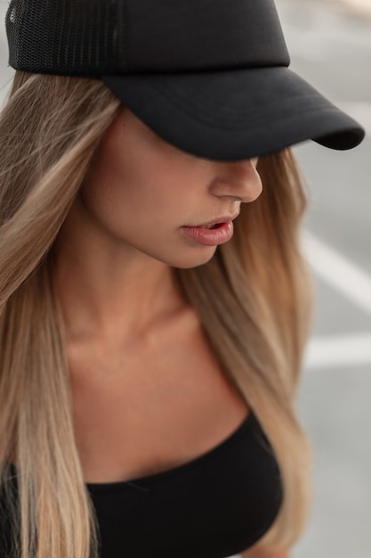 Fashionable urban portrait of a beautiful young woman in a black baseball cap and black T-shirt on the street, close-up