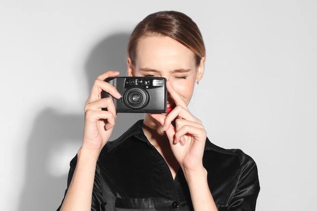 Fashionable woman in black dress with red lips taking photo with vintage camera isolated on white background