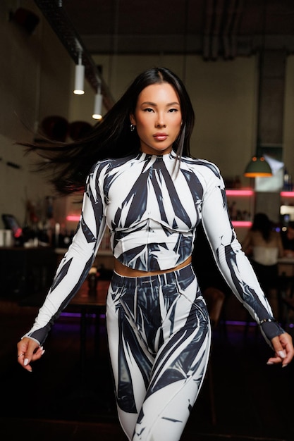 fashionable woman in black and white bodysuit posing indoors