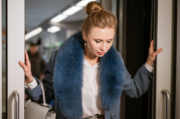 Fashionable woman in blue coat in train posing at camera