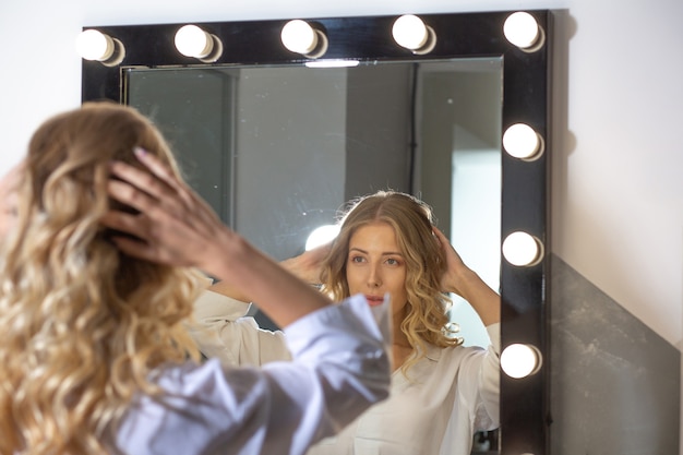 Photo fashionable woman client looking to her reflection in the mirror after hairstyling at beauty salon