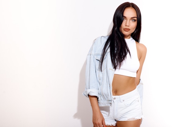 Fashionable woman in denim jacket and white shorts against white wall