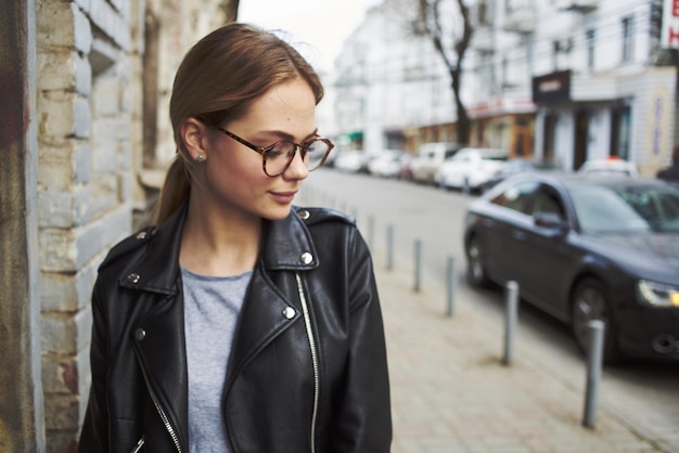 Fashionable woman in a leather jacket and glasses on the street and cars on the road High quality photo