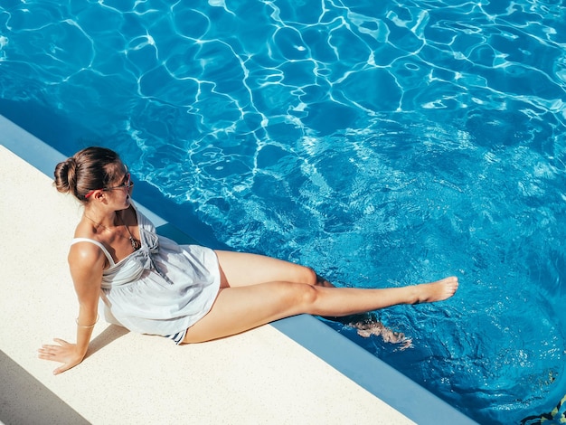 Fashionable woman sitting by the pool on the empty deck