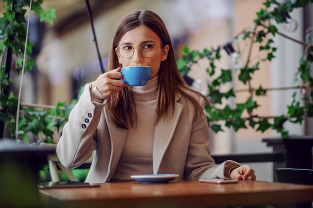 カフェテリアに座って、彼女のお気に入りのコーヒーを楽しんでいるファッショナブルな女性