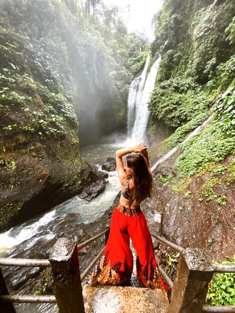 Foto donna alla moda in piedi vicino a una cascata in mezzo alle montagne