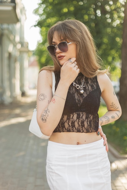 Fashionable woman in stylish summer outfit with a handbag and sunglasses walks in the city on a sunny day