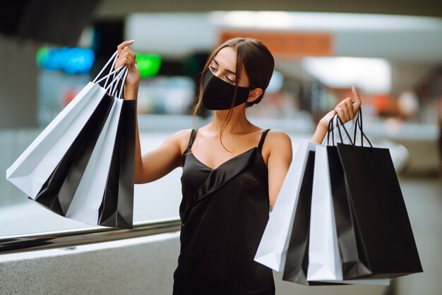 Fashionable woman wearing protective medical mask with shopping bags in the mall.