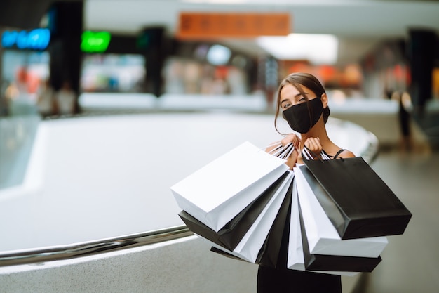 Fashionable woman wearing protective medical mask with shopping bags in the mall.