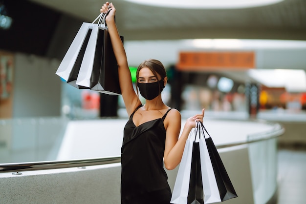 Fashionable woman wearing protective medical mask with shopping bags in the mall.