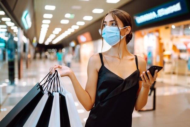 Fashionable woman wearing protective medical mask with shopping bags in the mall.