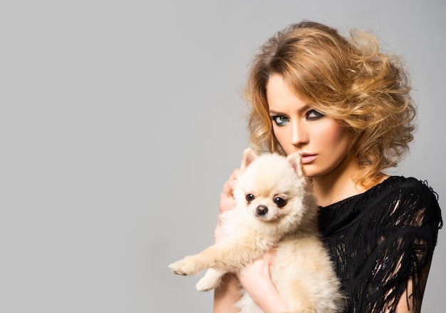 Fashionable woman with little dog. Dogs love. Beautiful young woman holding puppy on hands. National pet's day. Love animals.