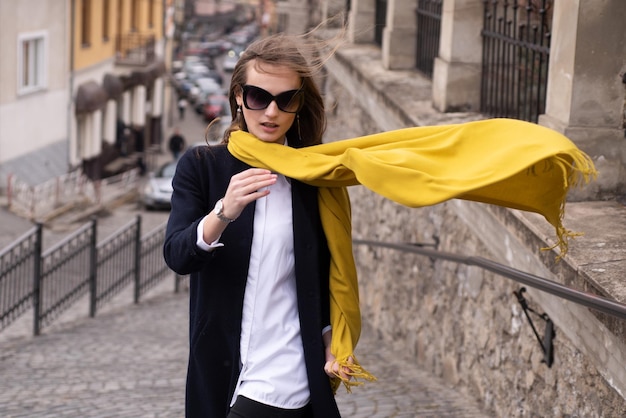 Fashionable woman with scarf blowing in wind on the street, fashion street style. Windy scarf.