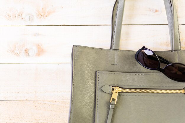 Fashionable womans leather tote with sunglasses on wood background.