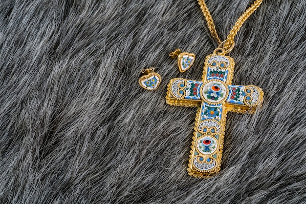 Fashionable women's gold plated cross or crucifix necklace and earrings on grey fake fur