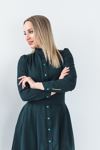 Fashionable young blonde woman in beautiful elegant dress posing at white studio.