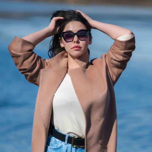 Fashionable young female with big breasts long hair plump lips and sunglasses dressed in beige coat