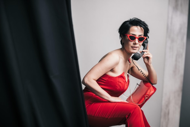 Foto una giovane donna alla moda con un vestito rosso che parla con un telefono giocattolo non funzionale.