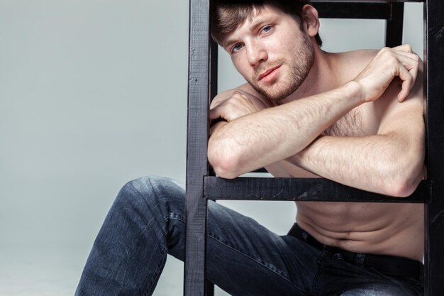 Fashionable young man posing with a ladder in studio