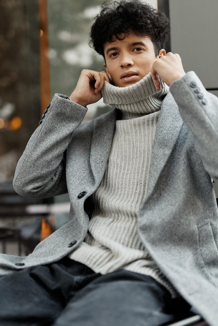 Photo 스웨터와 코트를 입은 유행의 젊은 남자가 손을 귀에 고 머리를 으로 기울여 벤치에 앉아 있습니다.