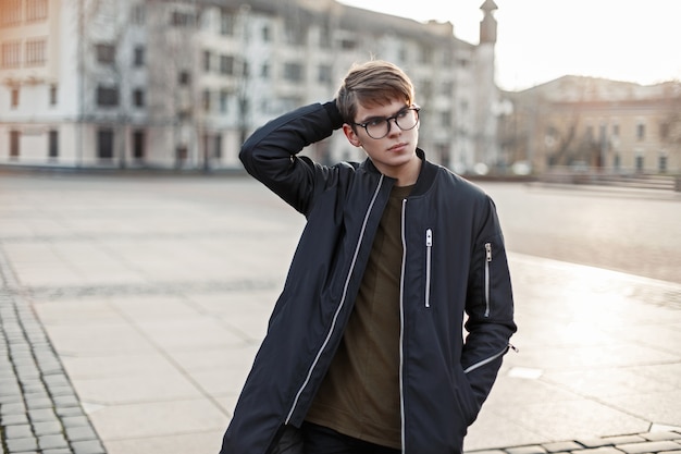 Fashionable young man with a haircut in a black jacket walking in the city