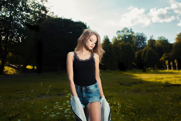 Photo fashionable young model posing in the park in a sunny day in summer