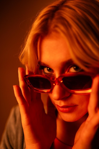 Photo fashionable young model wearing trendy sunglasses and stylish hat against orange background posing