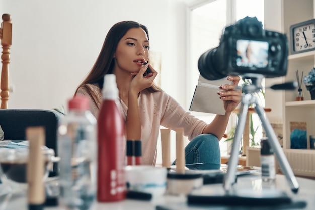 Fashionable young woman applying lipstick while making social media video