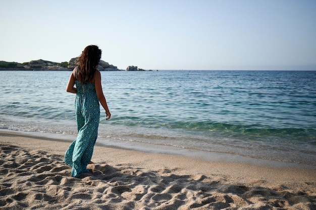 Foto giovane donna alla moda che sta sui capelli tranquilli della spiaggia che scorre godendosi la vacanza nella natura