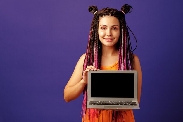 Studentessa alla moda giovane donna con lunghe trecce afro che tiene laptop su sfondo viola