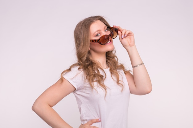 Fashionable young woman wearing t-shirt and sunglasses in white.