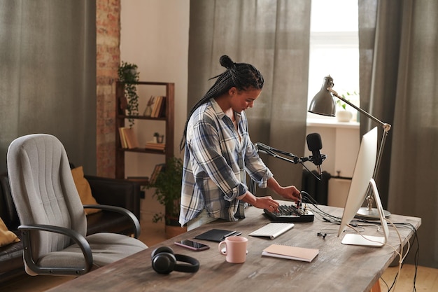 Fashionable young woman with afro braids standing at table in\
loft home office room setting and turn