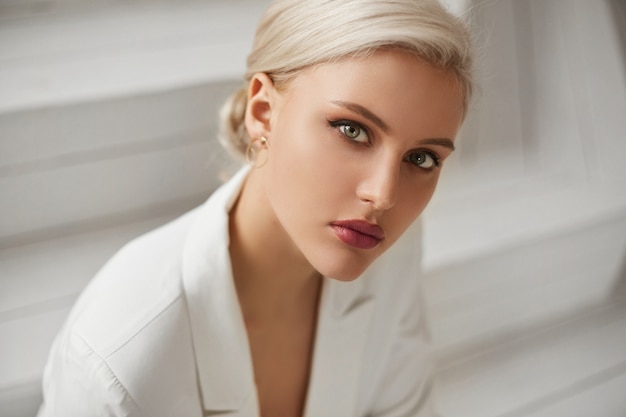 Photo a fashionable young woman with perfect blond hair and perfect trendy makeup in an elegant white suit