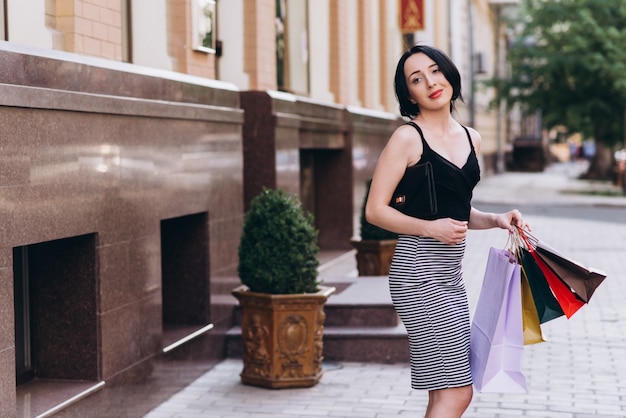 Fashionably dressed woman walking on the streets with colored shopping bags. Shopping concept