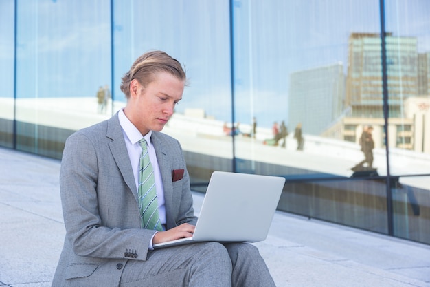 Fashioned young man working with laptop outdoor