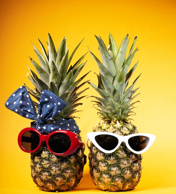 Fashionista in zonnebril op een gele achtergrond. twee ananas met glazen