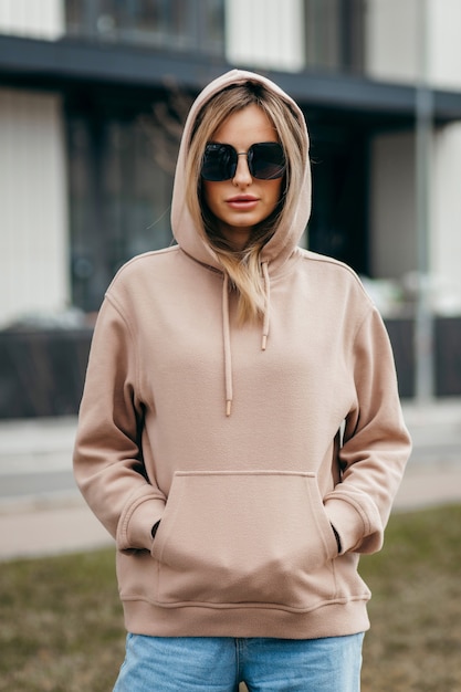 Fasion blonde vrouw in bruine oversized hoodie bril en spijkerbroek mockup voor logo of merkontwerp