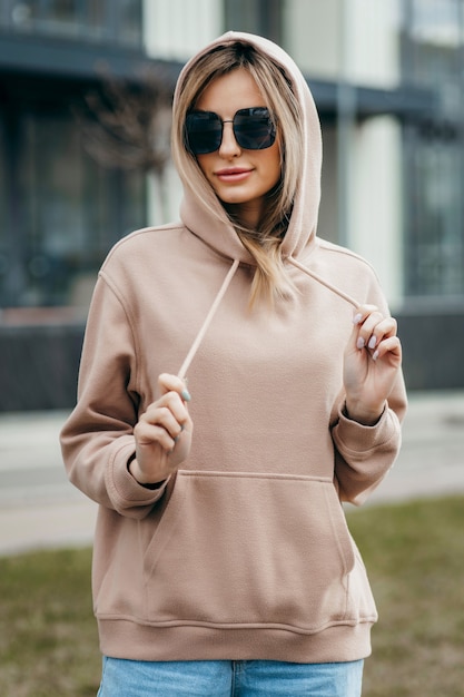 Fasion blonde vrouw in bruine oversized hoodie bril en spijkerbroek mockup voor logo of merkontwerp