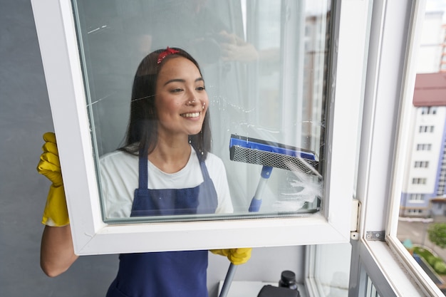 Photo fast and efficient. attractive young woman smiling while cleaning the window using squeegee. housework and housekeeping, cleaning service concept