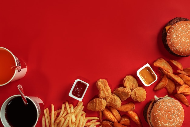 Вид сверху блюдо быстрого питания, мясной гамбургер, картофельные чипсы и стакан напитка на красном фоне, компо на вынос ...