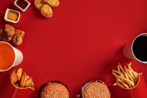 Fast food dish top view meat burger potato chips and glass of drink on red background takeaway compo...