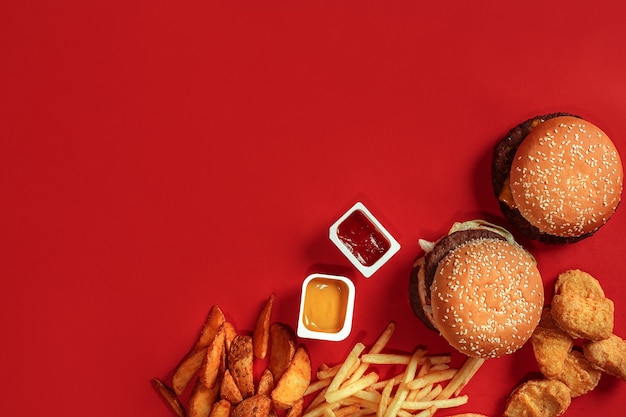 Fast food dish top view meat burger potato chips and nuggets on red background takeaway composition