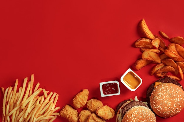 Fast food dish top view meat burger potato chips and nuggets on\
red background takeaway composition