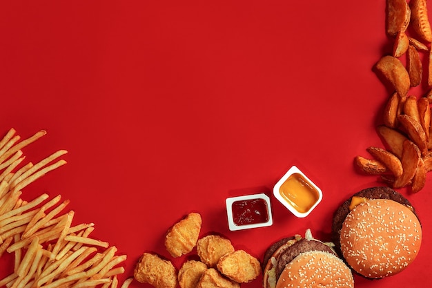 Вид сверху блюдо быстрого питания, мясной гамбургер, картофельные чипсы и наггетсы на красном фоне, композиция на вынос