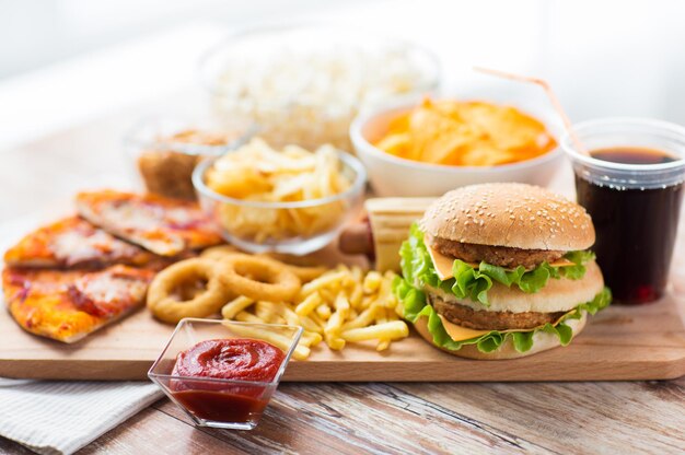 Fast food en ongezond eten concept - close-up van hamburger of cheeseburger, gefrituurde inktvisringen, frietjes, drankje en ketchup op houten tafel