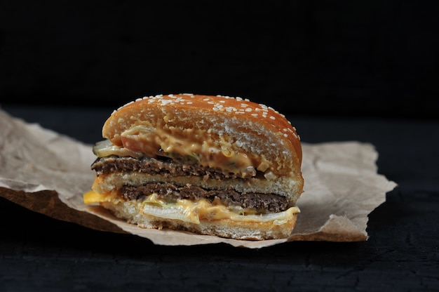 Fast food - in tweeën gesneden Hamburger met kaas en rundvlees op Kraft papier op zwarte houtskool achtergrond