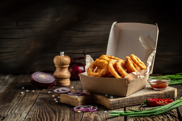 Fast food meal onion rings in paper box on wooden table