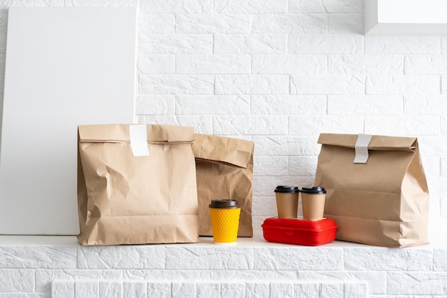 Fast food packaging set. Paper coffee cups in holder, food box, brown paper bag on the table.